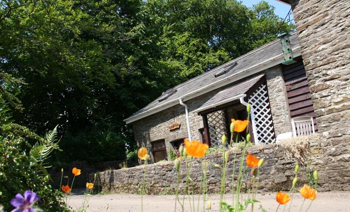 Stone cottage surrounded by lush greenery and colourful wildflowers under a blue sky.